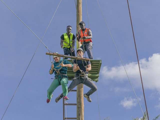 Two guests in harnesses swinging from the giant swing platform as guides watch