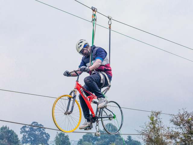 A guest in a helmet and harness riding a bicycle along a high cable