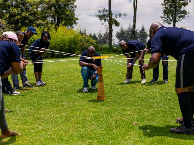 A team holding strings to stack wooden blocks together on the lawn