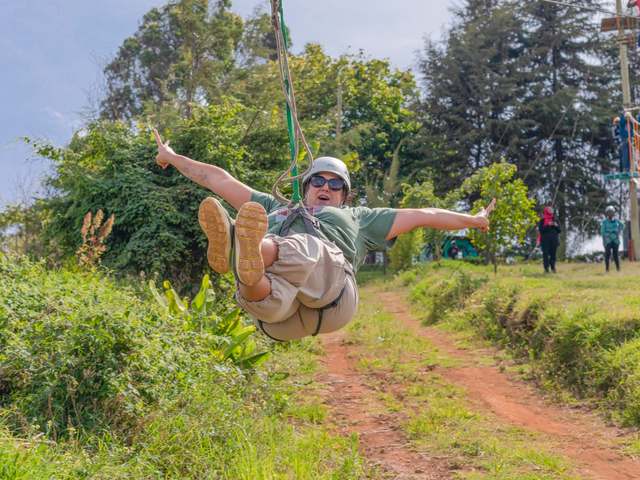 A guest in a harness ziplining over the park, arms out